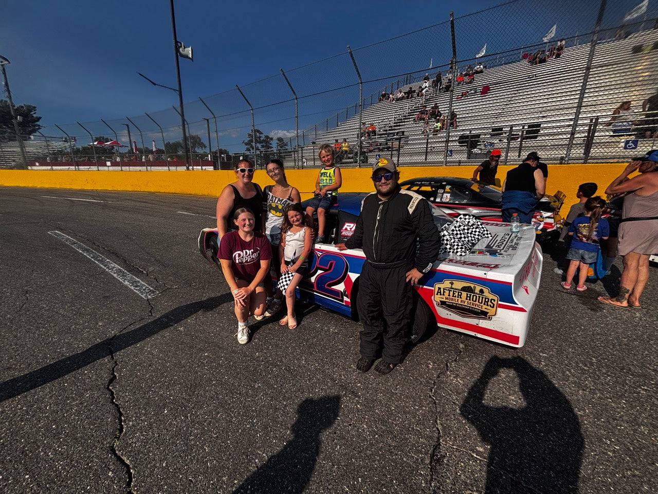 A group gathered beside the number 22 race car and checkered flags at the track