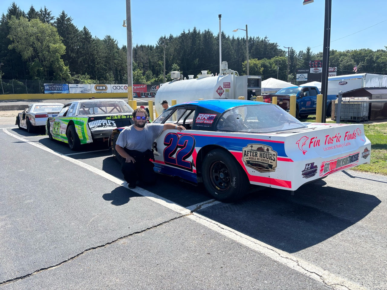 A person beside the white, blue and pink number 22 race car in the staging lane